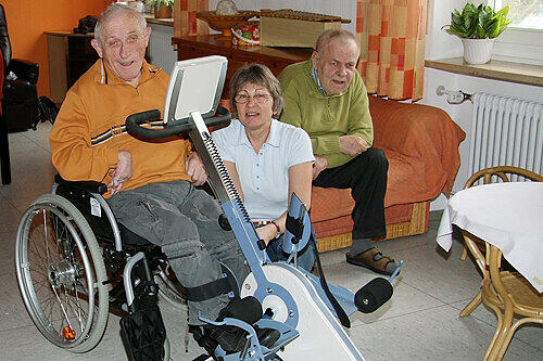 Eine Betreuerin hilft Leonhard Lutz am Fußtrainer. Der 78-Jährige ist von Geburt an halbseitig gelähmt und kann sein rechtes Bein nicht bewegen.
