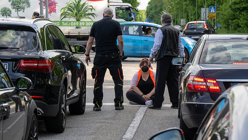 Aufgebrachte Autofahrer stehen vor einer auf der Straße sitzenden Klimaaktivistin. Aufgebrachte Autofahrer stehen vor einer auf der Straße sitzenden Klimaaktivistin.