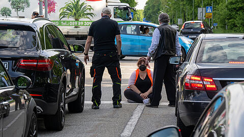 Aufgebrachte Autofahrer stehen vor einer auf der Straße sitzenden Klimaaktivistin.