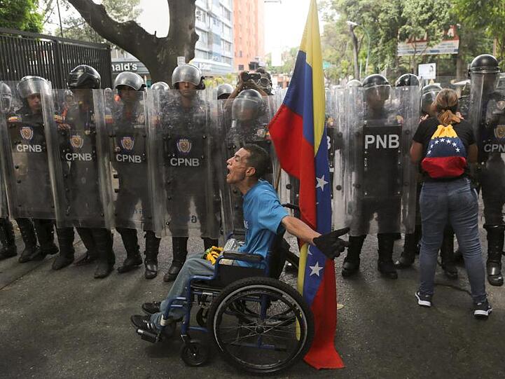 Ungleiche Machtverhältnisse: Ein Demonstrant im Rollstuhl beschimpft Polizisten, die ihn nicht zu einer Demonstration gegen Präsident Maduro durchlassen wollen.