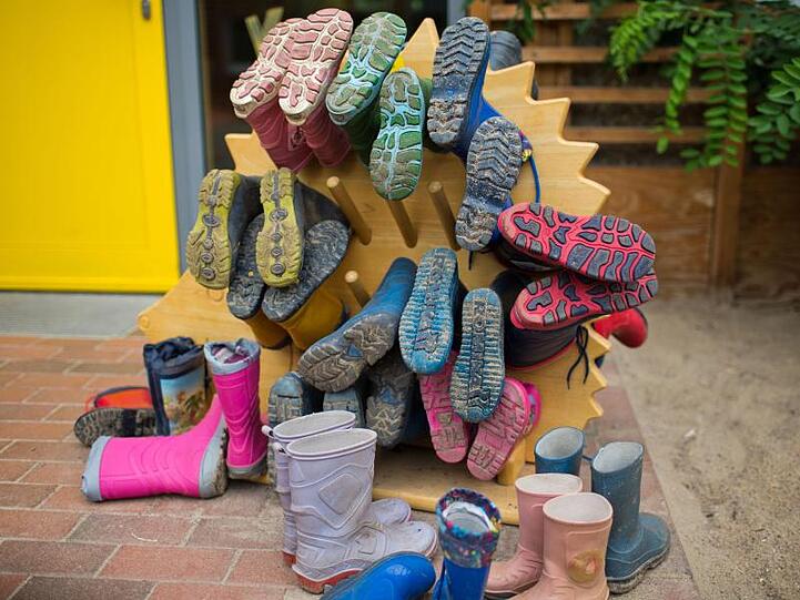 Kindergummistiefel hängen an einem Schuhhalter in einer Kindertagesstätte. Foto: Jens Büttner/Archiv