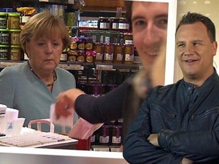 Ex-Dschungelkönig Peer Kusmagk (Mitte) lacht und staunt, als er beim Dreh zu Guido Maria Kretschmers (re.) Show plötzlich mit Angela Merkel (li.) an der Supermarkt-Kasse steht