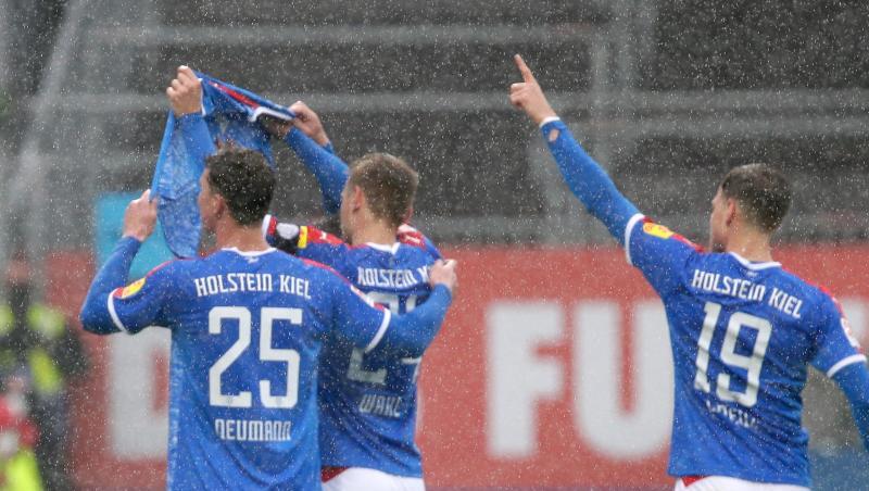 Die Kieler Spieler Phil Neumann (l-r), Hauke Wahl und Simon Lorenz halten nach dem Treffer zum 1:1 ein Trikot des verletzten Mannschaftskameraden Ahmet Arslan hoch.