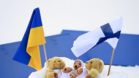 Fahnen der Ukraine und Finnlands in Kontiolahti neben den Weltcup-Maskottchen im Schnee.