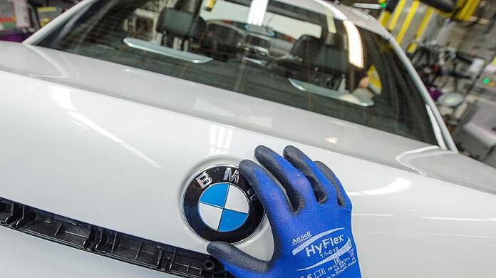 Ein Mitarbeiter montiert im BMW-Werk ein BMW-Emblem auf den Kofferraumdeckel eines Fahrzeugs.