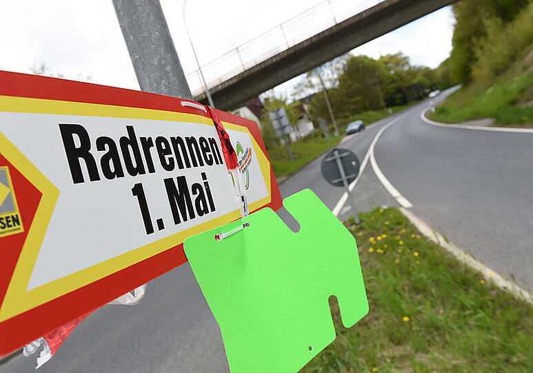 Ein Wegweiser mit der Aufschrift "Radrennen 1. Mai" ist an einem Kreisel in Oberursel an der Straße zum Sandplacken an einem Pfosten befestigt.