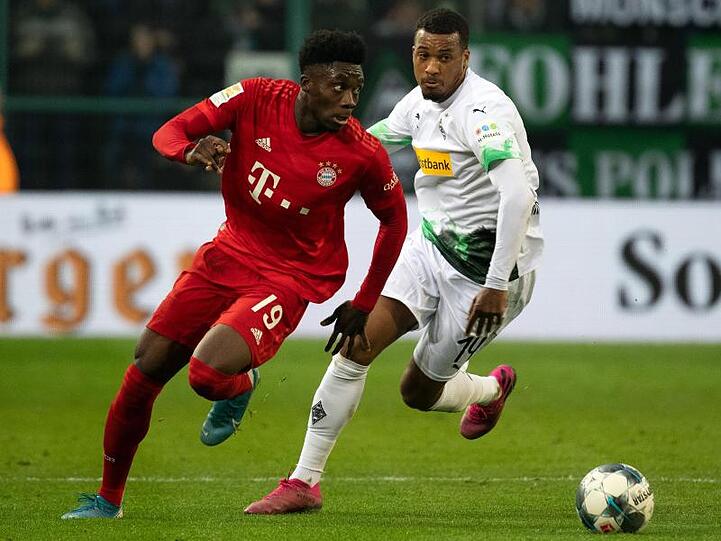 Bayerns Alphonso Davies und Mönchengladbachs Alassane Plea (l-r.) im Zweikampf um den Ball.