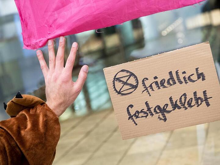 Thomas Nier, Aktivist der Bewegung Extinction-Rebellion klebt mit seiner Hand an einer Scheibe der Siemens-Konzernzentrale. Foto: Matthias Balk/dpa