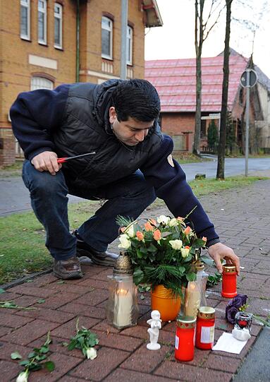 An einem mit Blumen und Kerzen geschmückten Bürgersteig stellt ein Mann am Dienstag in Stolzenau (Landkreis Nienburg) eine Kerze auf.