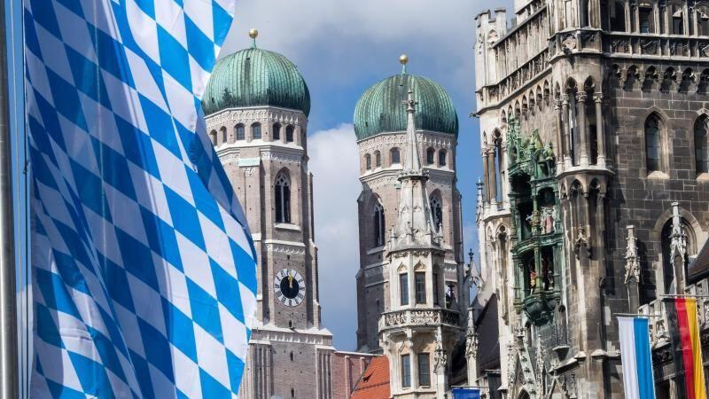 Die Türme der Frauenkirche (M), bayerische Fahnen und das Rathaus (r) in der Innenstadt. Foto: Peter Kneffel/Archivbild
