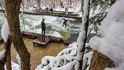 Die Welle ist zu jeder Jahreszeit ein Hotspot: Surfer stehen bei eisigen Temperaturen und Schnee mit ihren Brettern am Eisbach im Englischen Garten.
