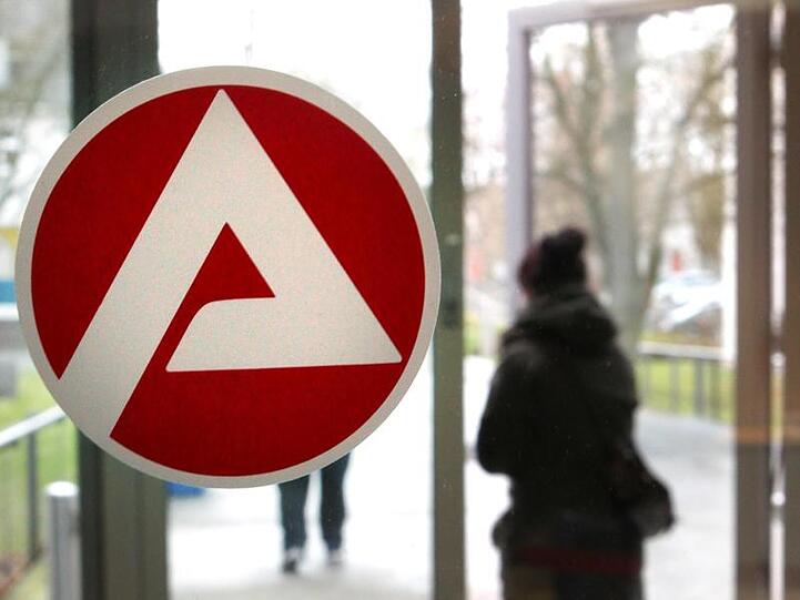 Eine Person verlässt die Agentur für Arbeit, im Vordergrund das Logo der Agentur. Foto: Bernd Wüstneck/Archivbild
