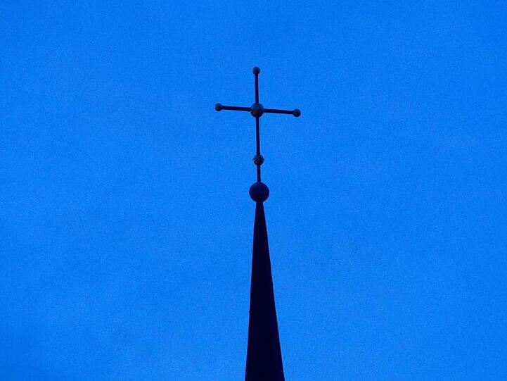 Ein Kreuz ist auf einer Kirchturmspitze zu sehen. Foto: Friso Gentsch/dpa/Symbolbild