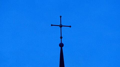 Ein Kreuz ist auf einer Kirchturmspitze zu sehen. Foto: Friso Gentsch/dpa/Symbolbild
