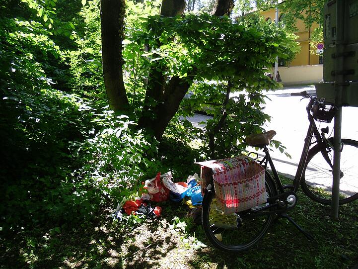 Direkt neben den Sachen steht ein Fahrrad mit seitlichen Taschen. Wurden deren Inhalt geplündert oder hat hier jemand seinen Mülleimer ausgekippt?