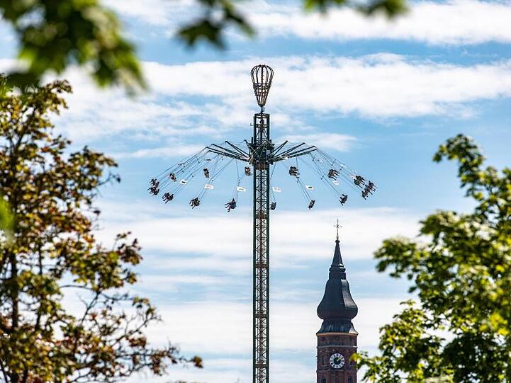 Mit einem Karussell fahren Besucher des Gäubodenvolksfestes vor dem Turm der Basilika St. Jakob. Foto: Armin Weigel