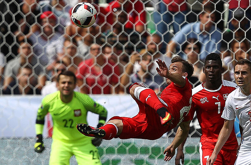 DER SEITFALLZIEHER VON XHERDAN SHAQIRI Ein Foto wie ein Gemälde. Xherdan Shaqiri schwebt hoch über seinem Schatten quer in der Luft, den Ball im Visier, das Bein bereit, gestreckt zu werden.