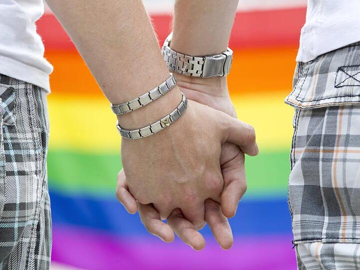 Zwei schwule Männer halten sich auf dem Straßenfest zum Christopher Street Day an den Händen.