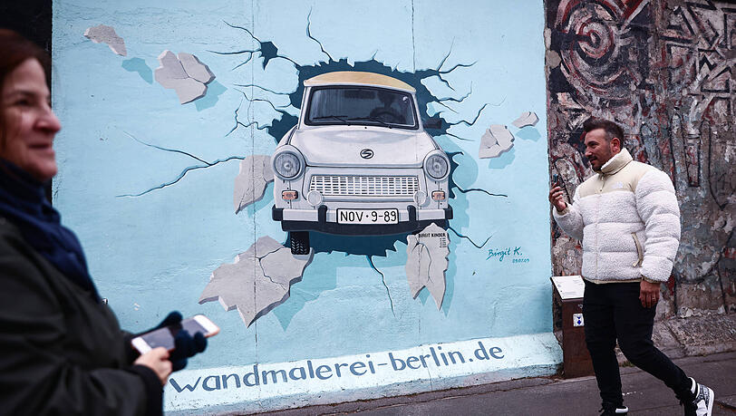 Menschen besuchen die Berliner East Side Gallery – eines der wenigen Überreste der Berliner Mauer, das nach der Wende von zahlreichen Künstlern bemalt wurden. Menschen besuchen die Berliner East Side Gallery – eines der wenigen Überreste der Berliner Mauer, das nach der Wende von zahlreichen Künstlern bemalt wurden.