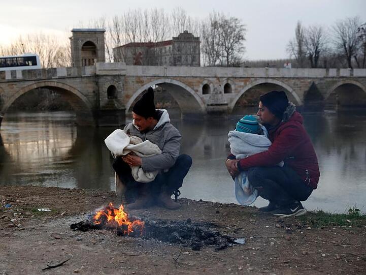 Migranten halten ihre Babys in den Armen neben einem Lagerfeuer am Ufer des Flusses nahe der türkisch-griechischen Grenze.