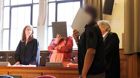 Die beiden Angeklagten verdecken im Gerichtssaal vor Sitzungsbeginn in Tübingen ihre Gesichter.