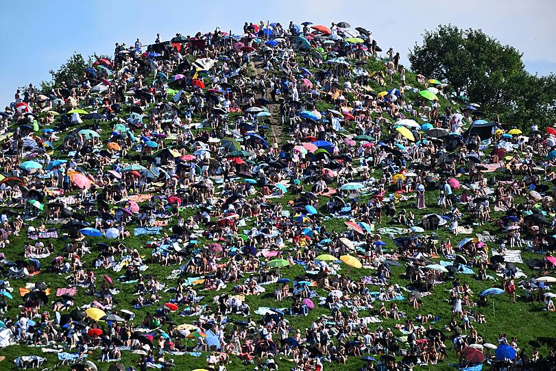 Fans sitzen auf dem Olympiaberg im Olympiapark und warten bei Sonnenschein auf den Beginn des Taylor Swift Konzerts.