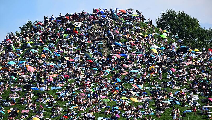 Fans sitzen auf dem Olympiaberg im Olympiapark und warten bei Sonnenschein auf den Beginn des Taylor Swift Konzerts.