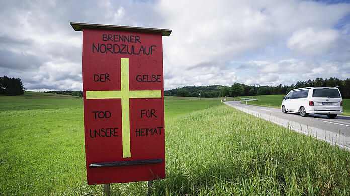Ein Protestschild mit der Aufschrift "Brenner Nordzulauf - Der gelbe Tod für unsere Heimat" einer Bürgerinitiative steht auf einer Wiese der geplanten Bahntrasse.