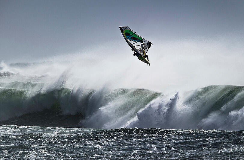 Ein Windsurfer fliegt über die Wellen (Motivbild).