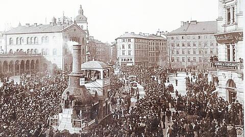 Faschingszug 1896: Der Faschingswagen "Zum Kamin" wird von Pferden über den Bahnhofsplatz am Hauptbahnhof (l.) gezogen.