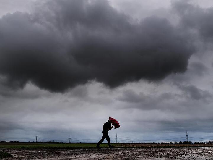 Ein Spaziergänger geht beistarkem Regen über einen Feldweg mit seinem Schirm. Foto: Federico Gambarini/Archivbild