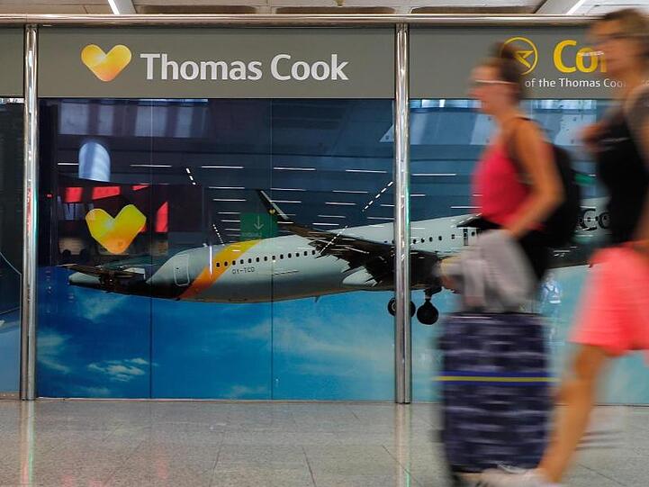 Passagiere neben einem großen Werbeschild von Thomas Cook am Flughafen von Palma de Mallorca.