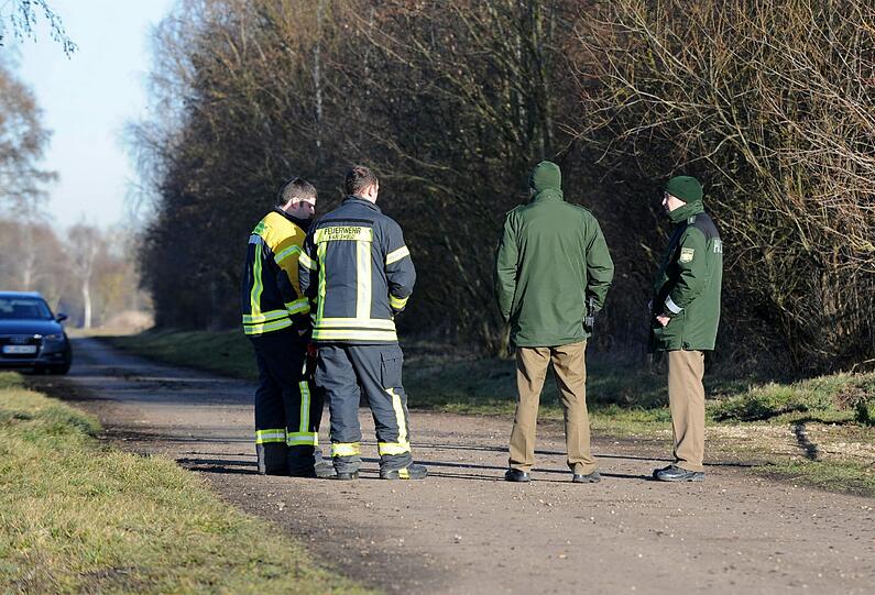 Zwei Feuerwehrmänner und zwei Polizisten stehen am Montag auf einem Feldweg am Ufer des Rathei-Weihers zwischen Zell und Karlshuld im Landkreis Neuburg-Schrobenhausen.