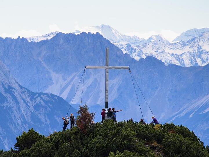 Wanderer stehten neben dem Gipfelkreuz vom Martinskopf bei Walchensee. Foto: Matthias Balk/dpa/Archivbild