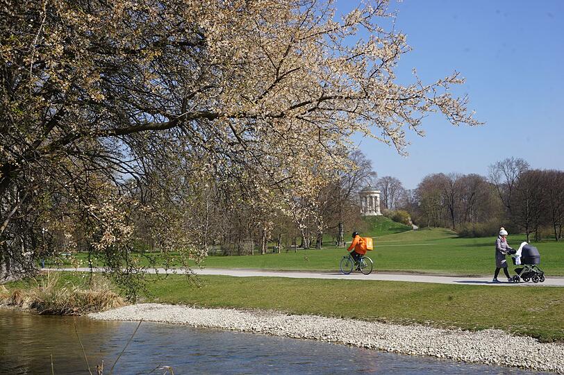 Ein radfahrender Lieferant und eine Mutter mit Kinderwagen im Englischen Garten.