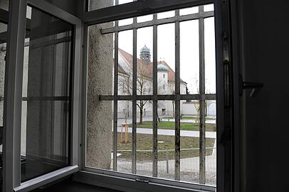 Hinter-Gitter-Blick vom Gefängnisflur nach draußen in den Innenhof Hinter-Gitter-Blick vom Gefängnisflur nach draußen in den Innenhof