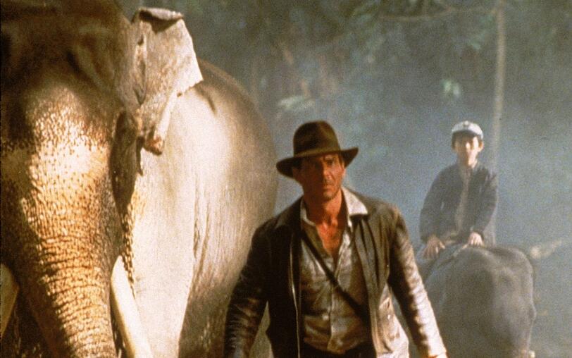 Auf Elefanten machen sich Indy (Harrison Ford, links) und Shorty (Jonathan Ke Quan) auf den Weg zum Palast des Maharadschas von Pankot. Auf Elefanten machen sich Indy (Harrison Ford, links) und Shorty (Jonathan Ke Quan) auf den Weg zum Palast des Maharadschas von Pankot.