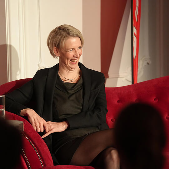 Adrian Prechtel im Gespräch mit Bürgermeisterin Katrin Habenschaden auf dem roten Sofa (von Möbel Höffner) in München.