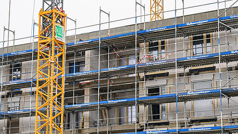 An einem im Bau befindlichen Geb&auml;ude des sozialen Wohnungsbaus sind Fassadenelemente montiert, das Haus ist von einem Bauger&uuml;st umgeben. (Symbolbild)
