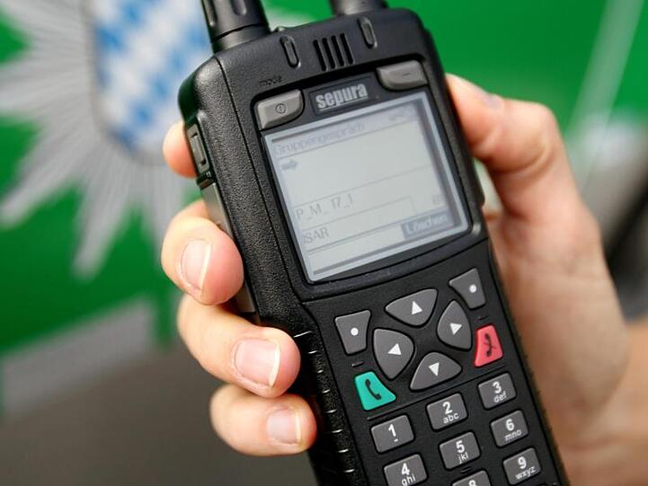 Eine Polizeibeamtin hält ein Digitalfunkgerät vor ein Polizeiauto. Foto: Lukas Barth/Archivbild