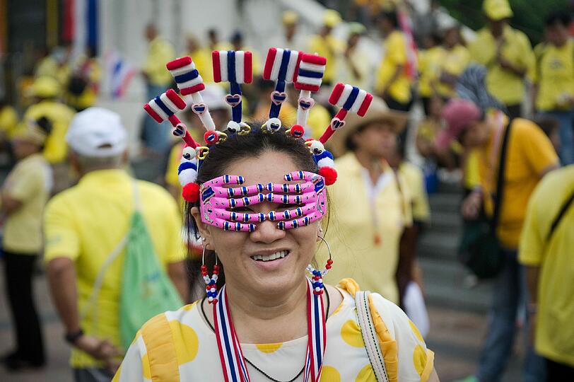 Festtage in Thailand: Tausende Menschen gehen auf die Straßen und feiern den Amtsantritt von König Bhumibol Adulyade vor 64 Jahren. Die Frau auf dem Foto hüllt sich in Miniatur-Thailandflaggen.