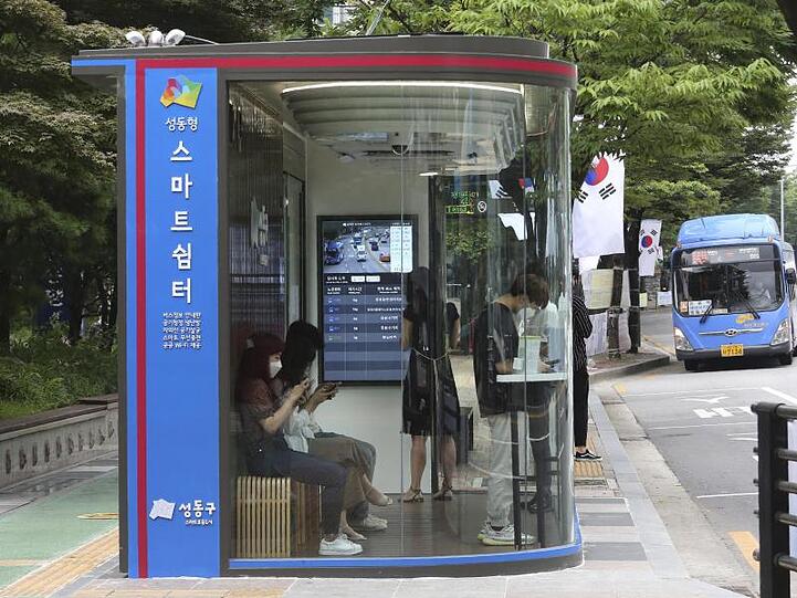 Menschen warten in Seoul in einem "smarten" Wartehäuschen auf den Bus.