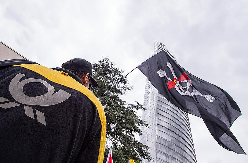 Ein Mitarbeiter der Post demonstriert am in Bonn mit einer Piratenfahne vor dem Post-Tower.
