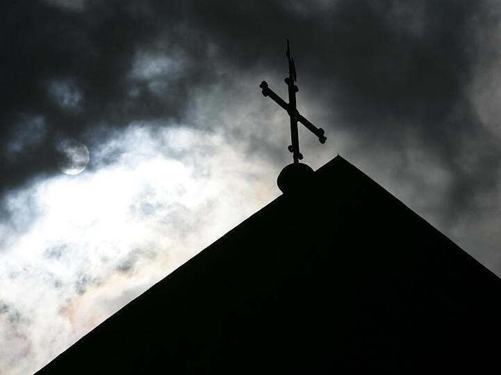 Kirchturmspitze mit Kreuz im Gegenlicht. Foto: Friso Gentsch/dpa/Symbolbild