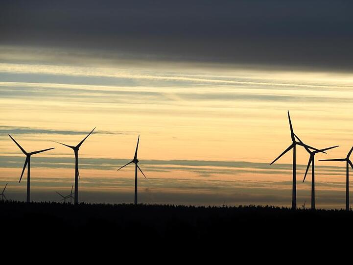 Windkraftanlagen stehen im Morgenlicht unter einem dunklen Wolkenstreifen.