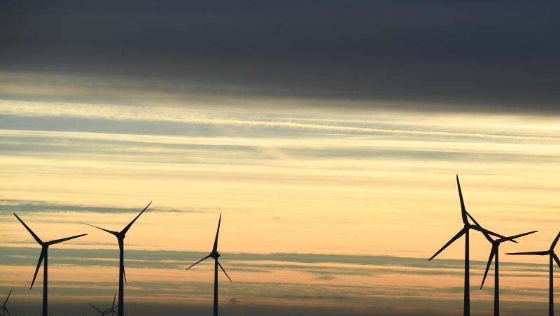 Windkraftanlagen stehen im Morgenlicht unter einem dunklen Wolkenstreifen. Windkraftanlagen stehen im Morgenlicht unter einem dunklen Wolkenstreifen.