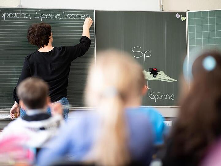 Eine Lehrerin schreibt in einer Grundschule Wörter mit "Sp" am Anfang an eine Tafel. Foto: Sebastian Gollnow/Archivbild