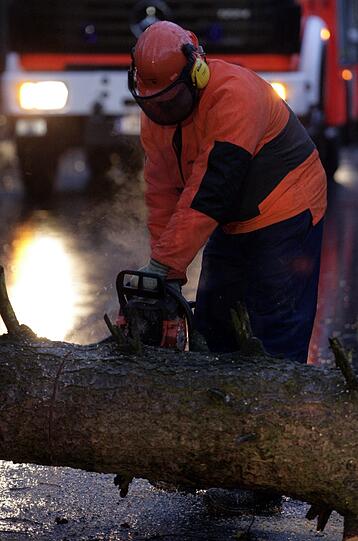 Ein Feuerwehrmann zersägt am Donnerstag (05.01.2012) in Hamburg einen auf die Straße gestürzten Baum. Sturmtief «Andrea» sorgt für reichlich Sturm und Regen im Norden.