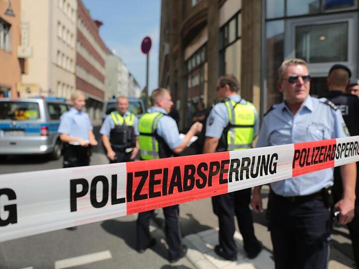 Polizisten stehen vor einem Wohngebäude eines der mutmaßlichen Gefährder in der Kölner Innenstadt hinter einem Absperrband.