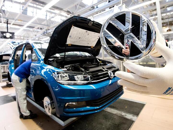 Ein Mitarbeiter zeigt ein VW Logo kurz vor Einbau in einen Volkswagen Touran in der Endmontage im VW Werk.